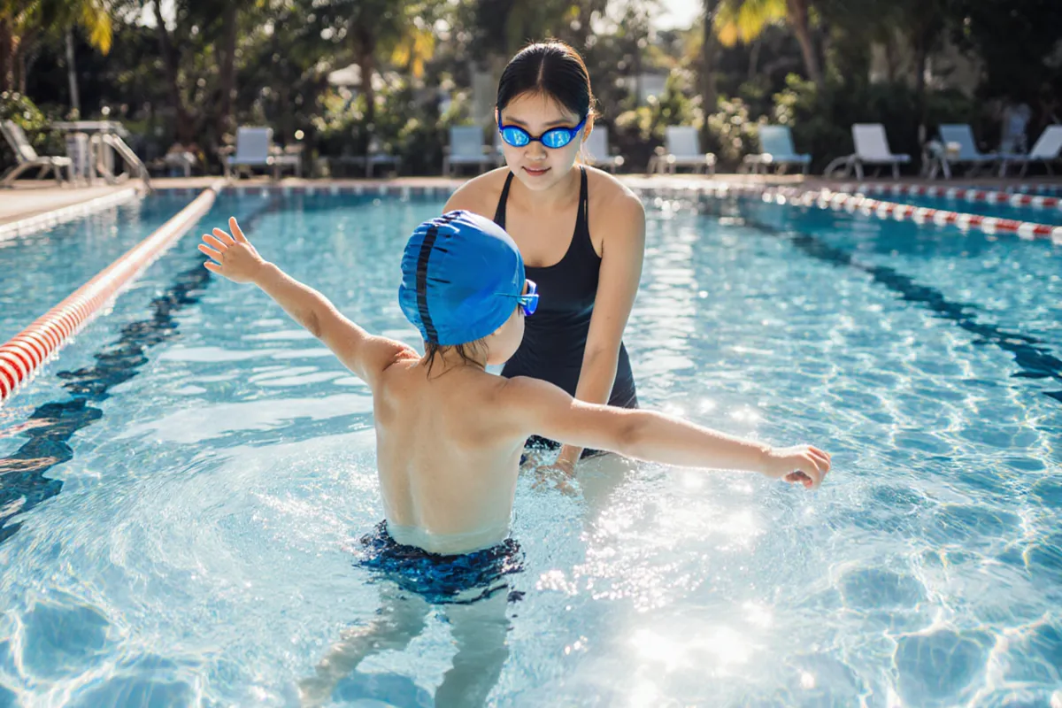 Swimming coach guiding Asian child with freestyle technique at outdoor ActiveSG pool Singapore