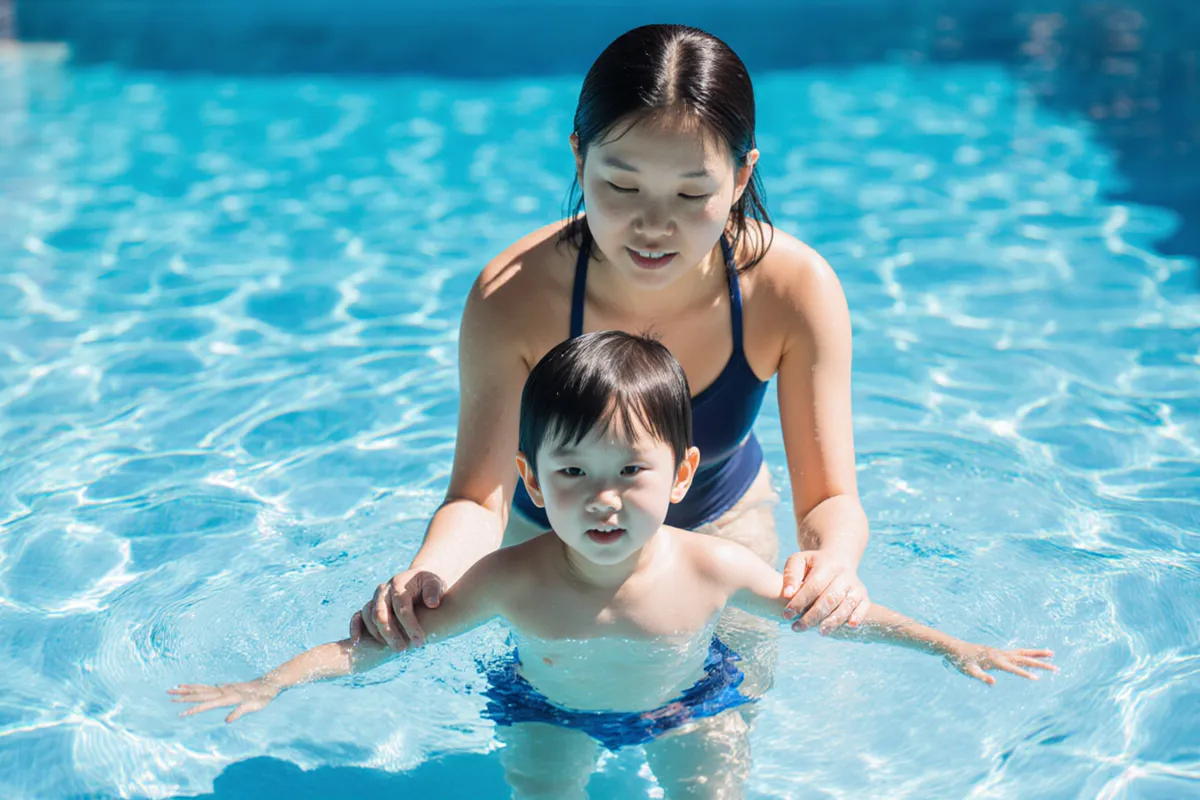 Coach guiding child through float position at pool