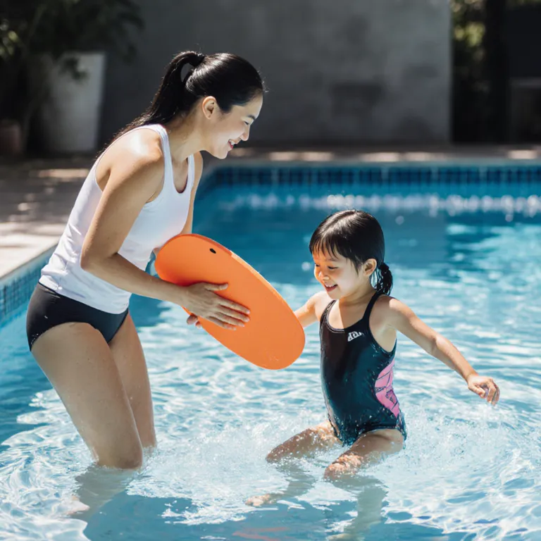 Swim coach guiding a young girl with a kickboard during a private lesson